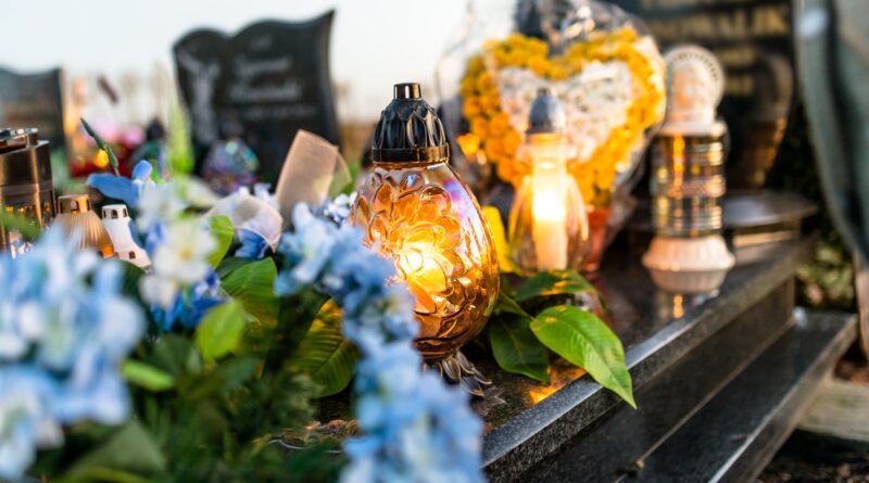 Artificial and real flowers and lit candles lying on the tombstone in the cemetery.