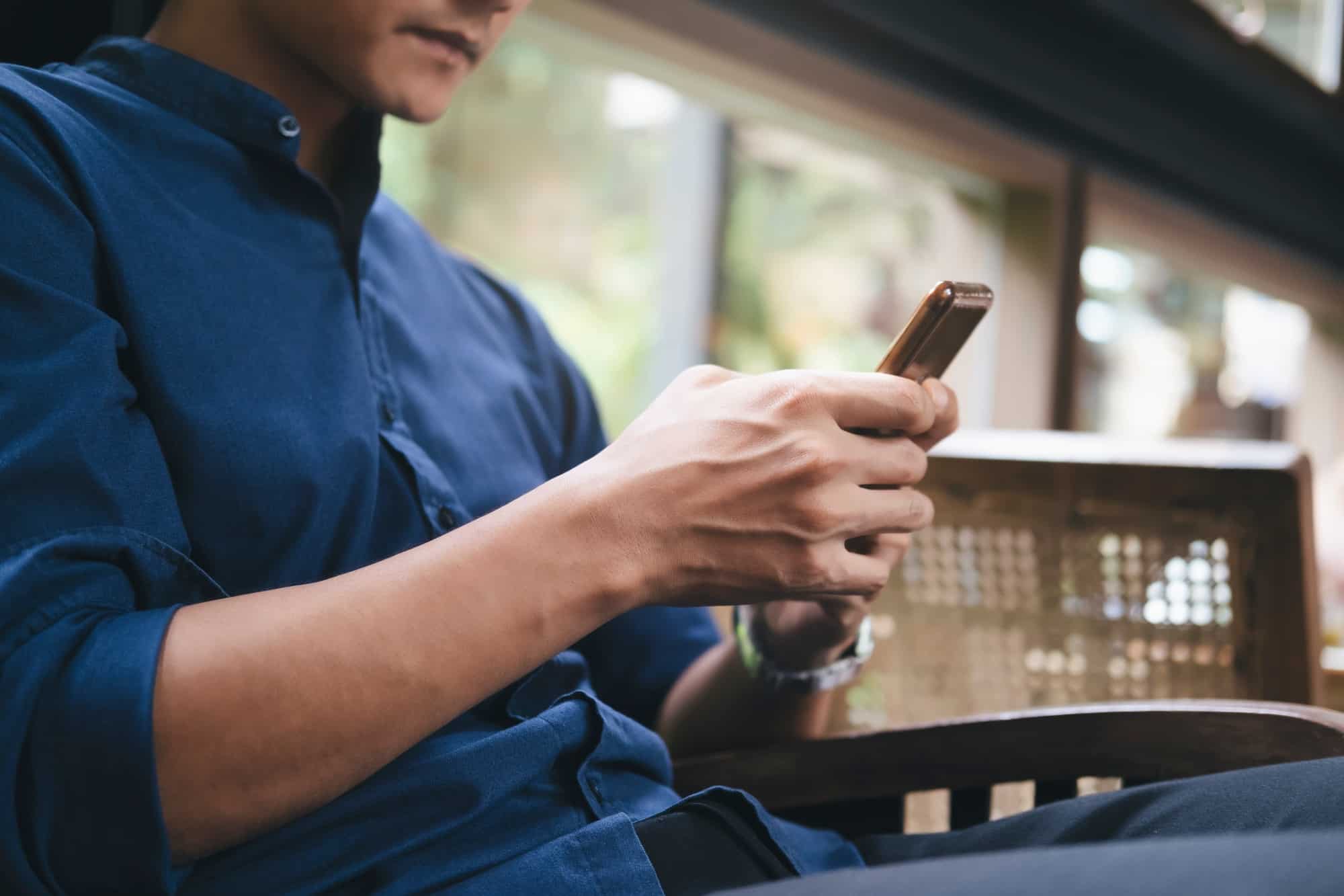 Businessman holding a cell phone and writing sms message in cafe.