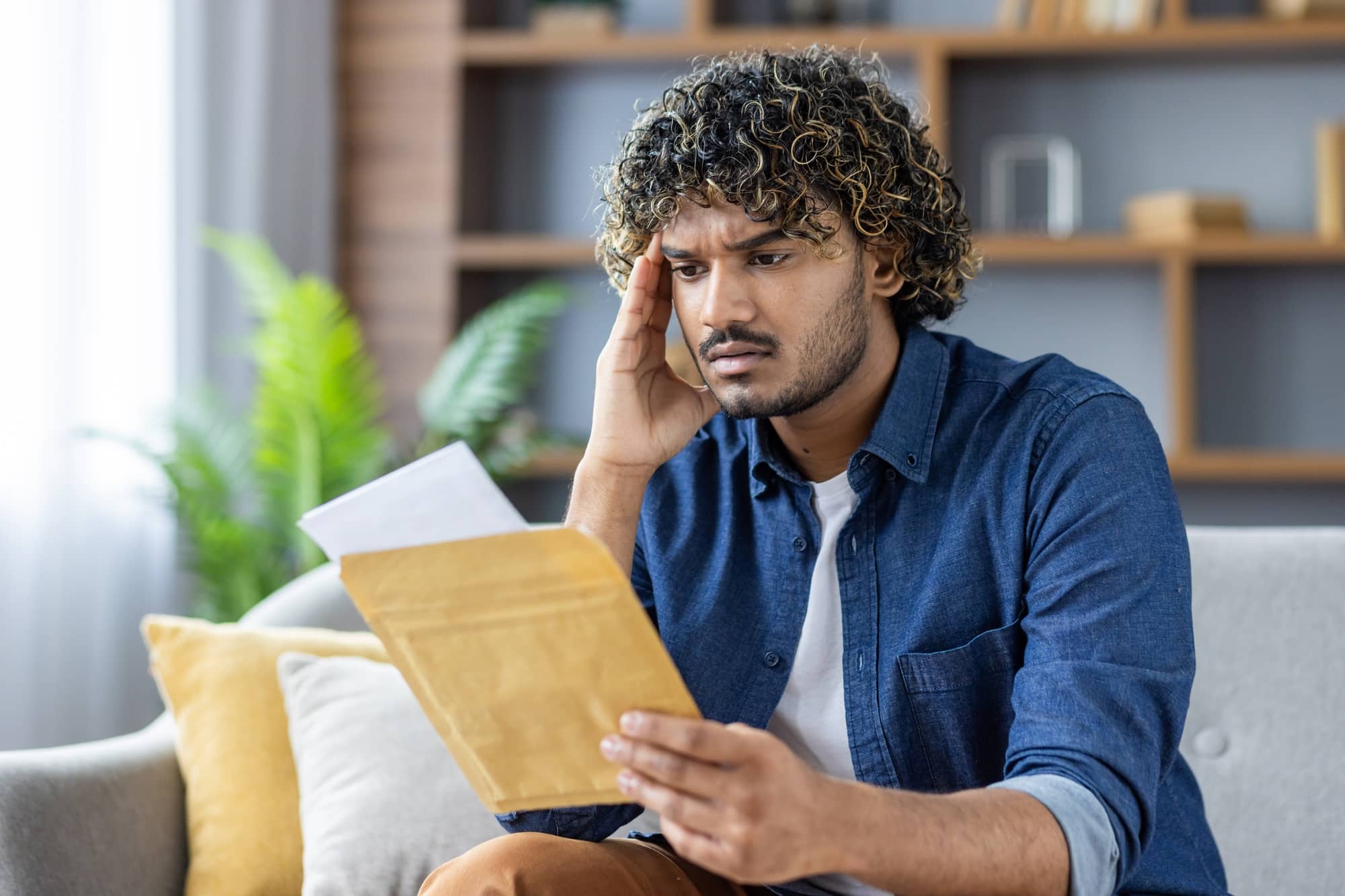 Concerned man reading a letter while sitting on a couch at home