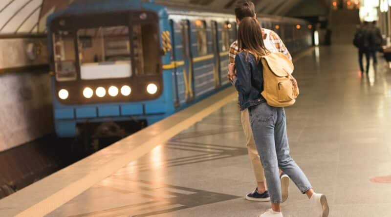 rear view of stylish couple of travelers with backpacks at metro station