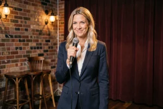 Humoriste française blonde sur scène dans un club de comédie intimiste, microphone en main avec un sourire assuré